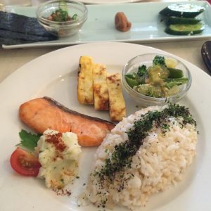 Japanese breakfast (clockwise from top left): nori, natto, salted plum, pickles, broccoli and snap peas with tofu in miso dressing, rice, potato salad, grilled salmon, omelette